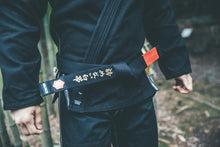 Lade das Bild in den Galerie-Viewer, Cinturón Kanji  &quot;Un cinturón blanco que nunca se rindió&quot; - Negro con barra Roja - StockBJJ
